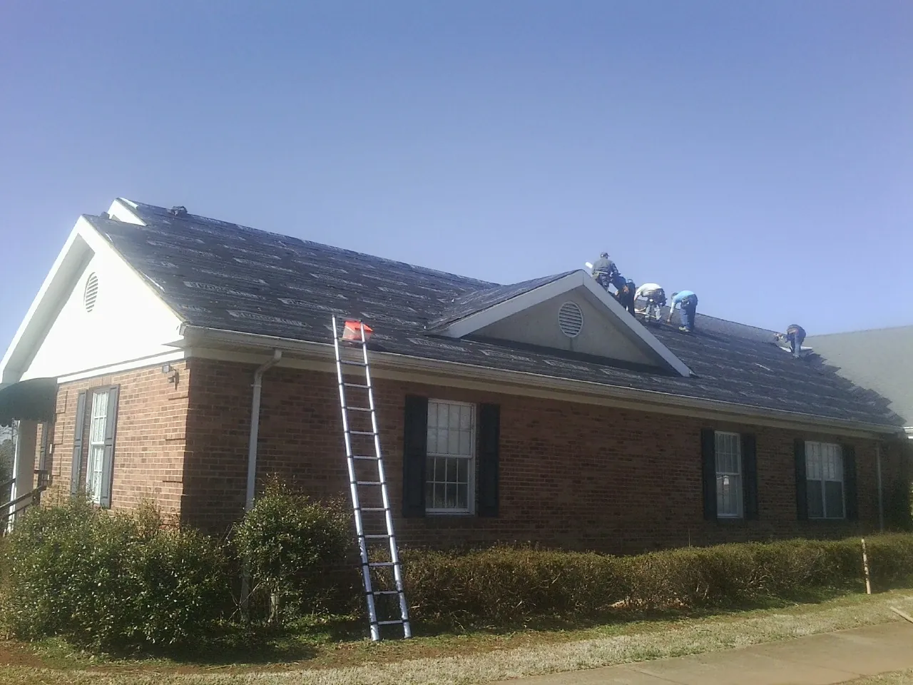 Crew tearing shingles off a brick ranch roof with a ladder set — Metal Roof Repair work by our crew in Castleford