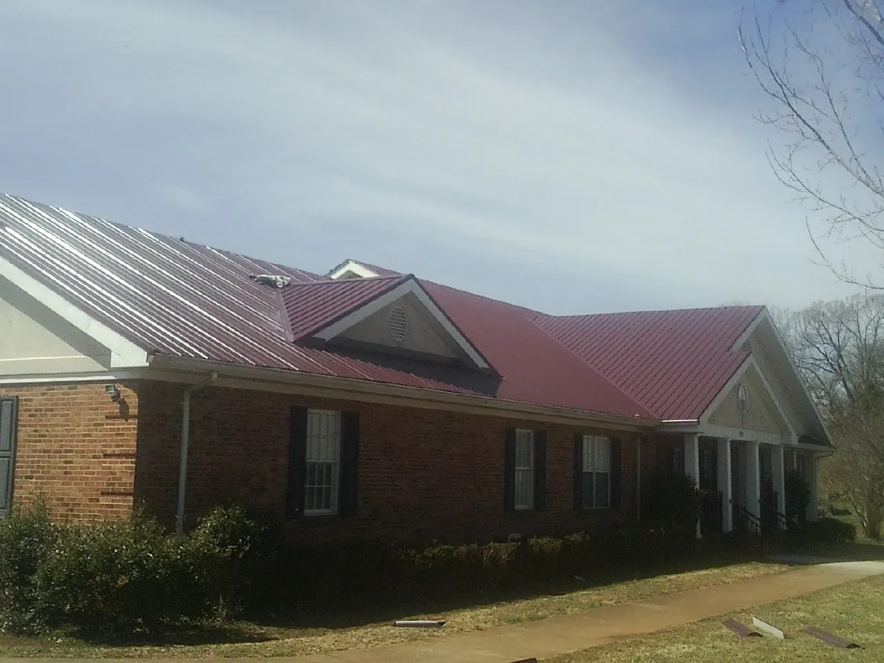 Red metal roof with gabled entries on a long brick building, from a Hail Damage Roof Repair job in Castleford