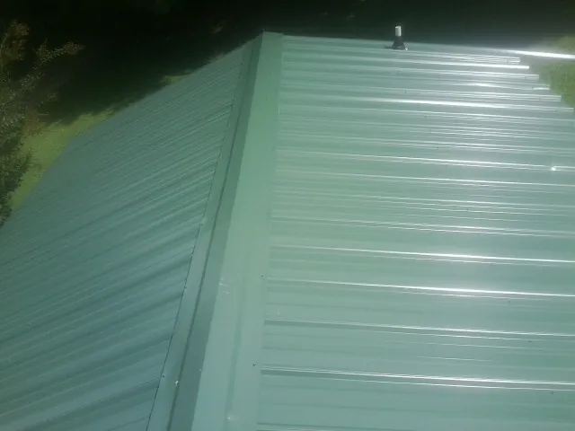 New green metal panels meeting at the ridge of a roof — Flat Roof Repair work by our crew in Castleford