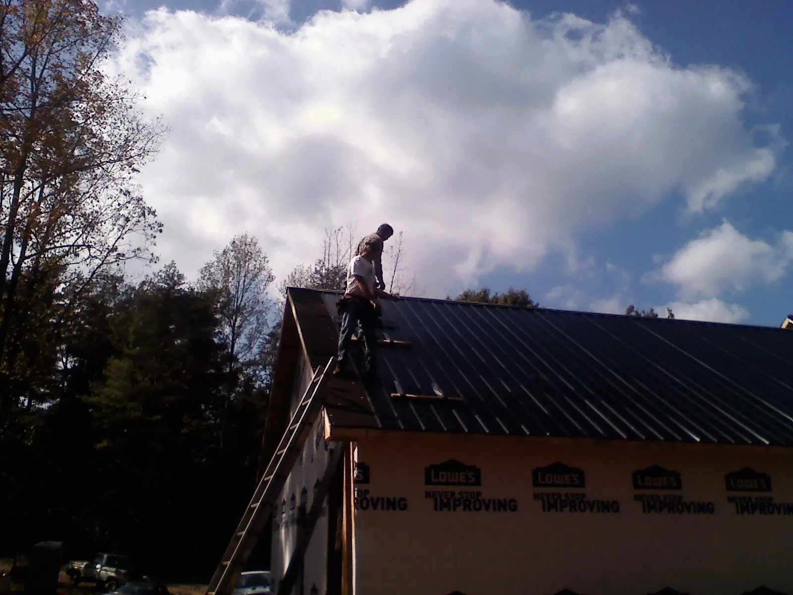 Roofer fastening dark metal panels high against a cloudy sky, from a Roof Inspection job in Castleford