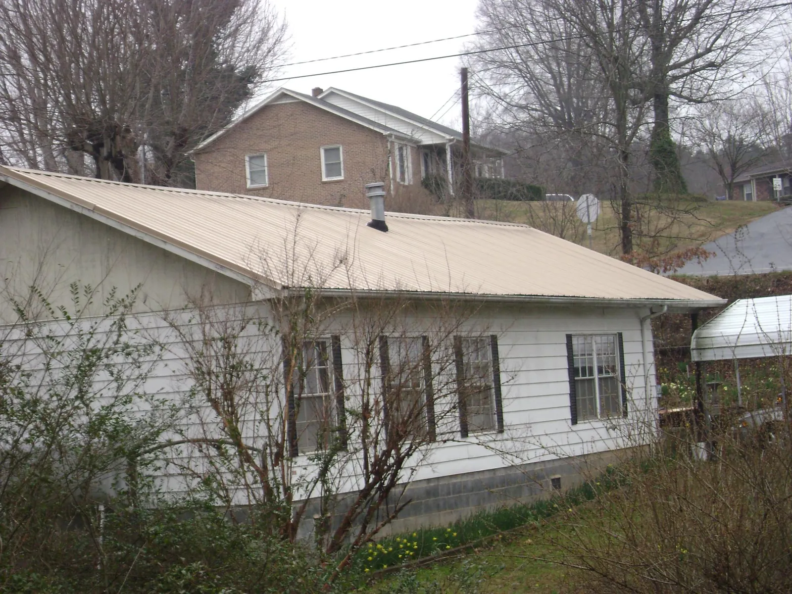 Tan metal roof on a white sided house set into a hillside — Commercial Roofing by Roofing Brothers in Castleford